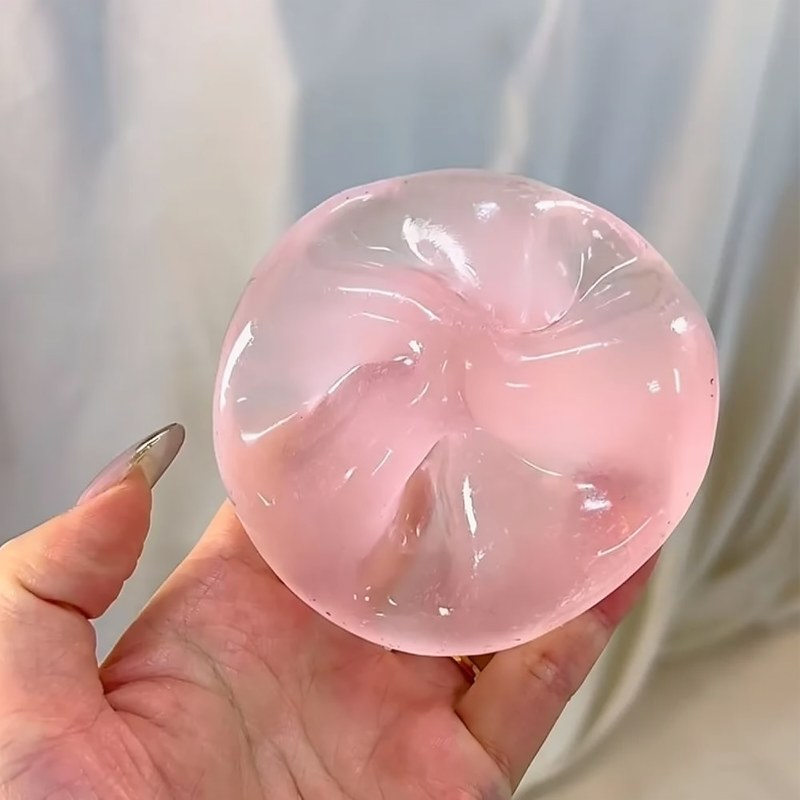 A hand holds a translucent pink stress ball with a slow-rise texture against a light background.
