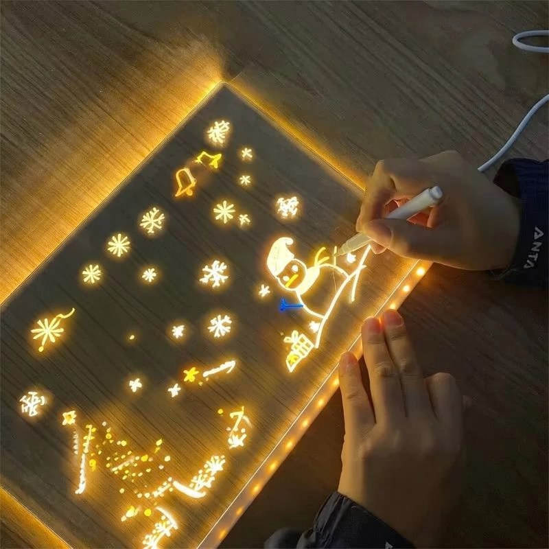 A hand draws on a glowing LED drawing board with colored pens, creating bright light patterns.