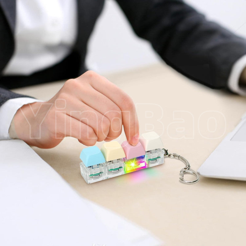 A set of colorful LED macaron keyboard fidget toys attached to a keychain, resting on a light-colored surface.